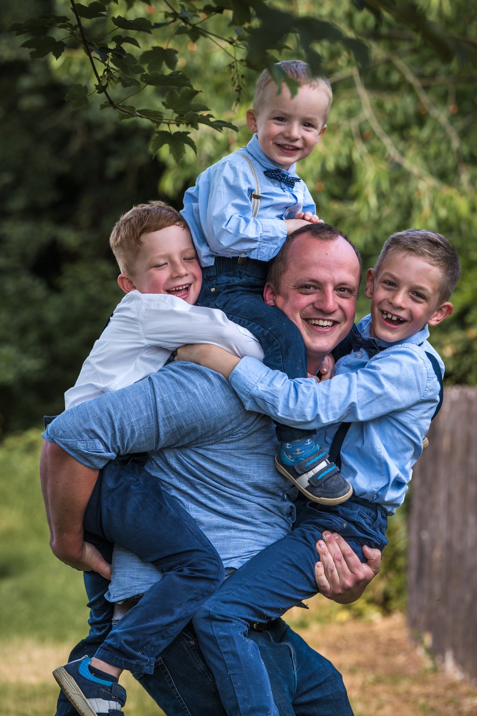 Papa trägt lachend drei Jungs gleichzeitig auf Rücken und Armen