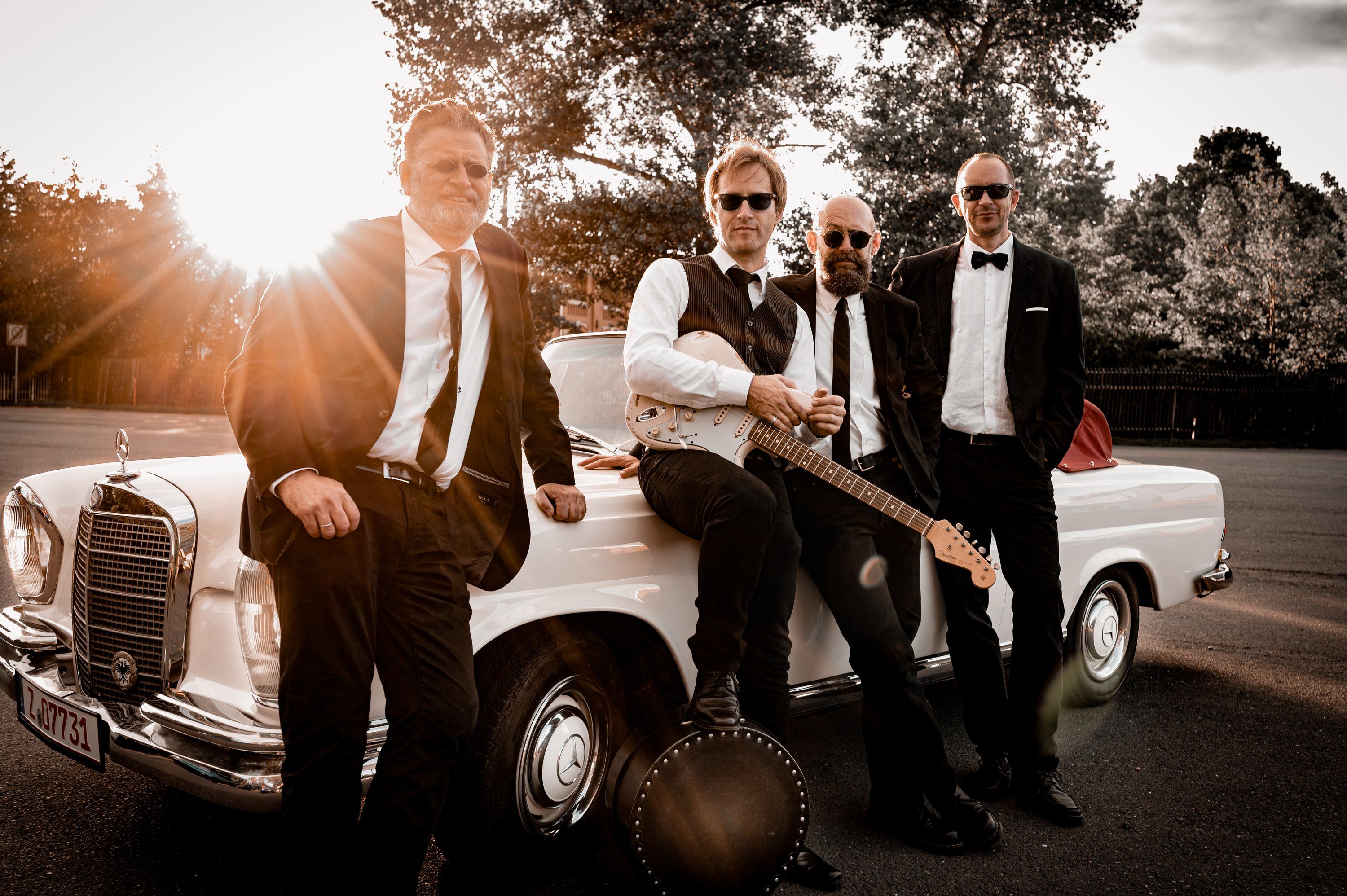 Band lehnt im Gegenlicht an einem weißen Oldtimer-Cabrio